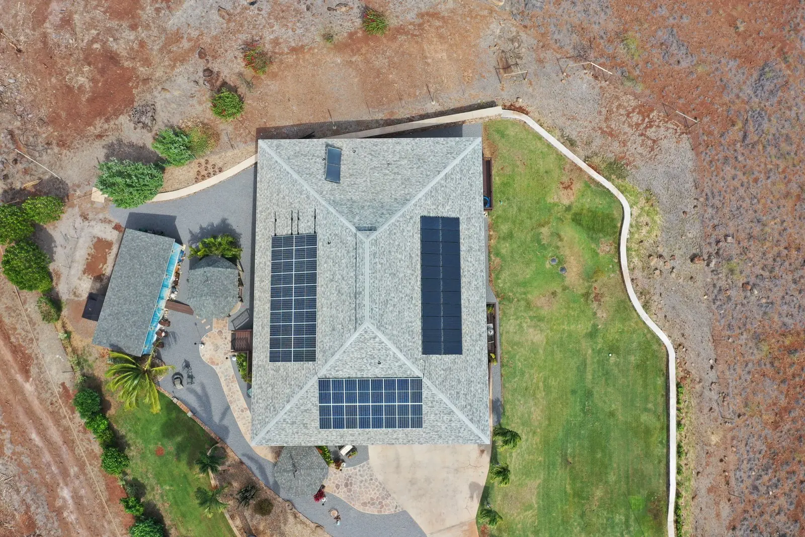 Overhead view of a home with rooftop solar surrounded by red Molokaʻi earth